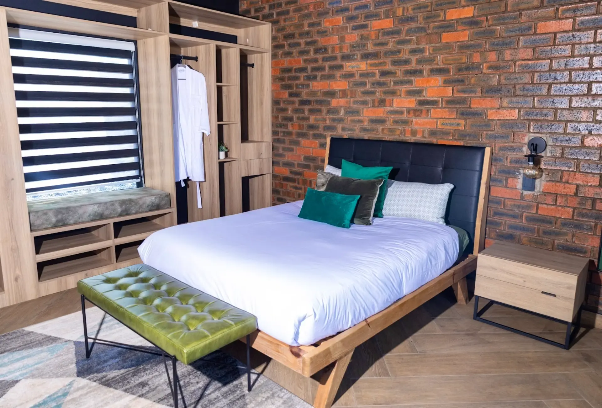 Villa bedroom with exposed brick feature wall, oak bed and green velvet accents