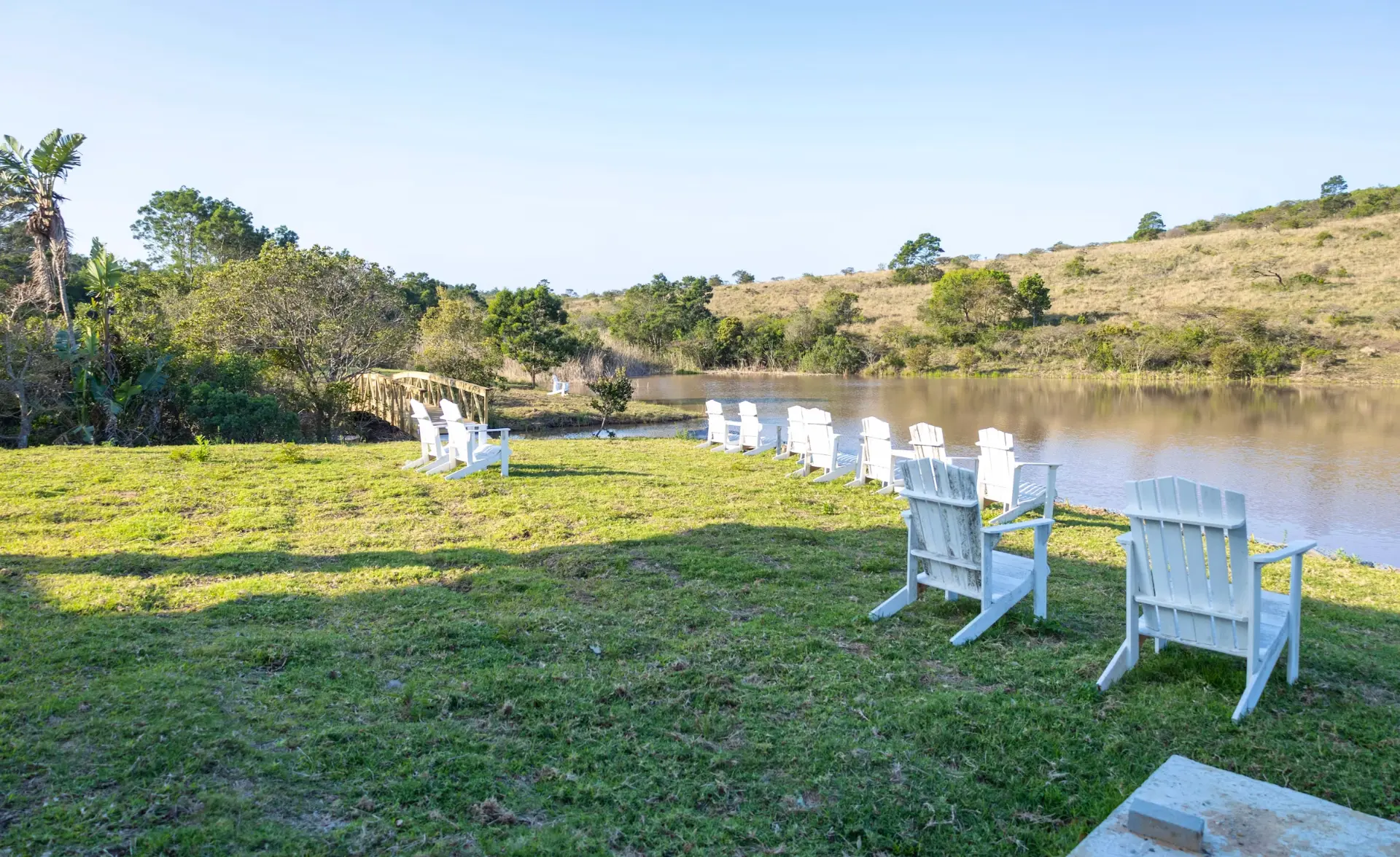 White deck chairs on the lawn facing the farm dam